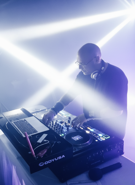 Cedric Le DJ en live – Set Funky House Cedric Le DJ en pleine performance derrière ses platines, sous des faisceaux lumineux blancs et violets, lors d’une soirée dansante en régio